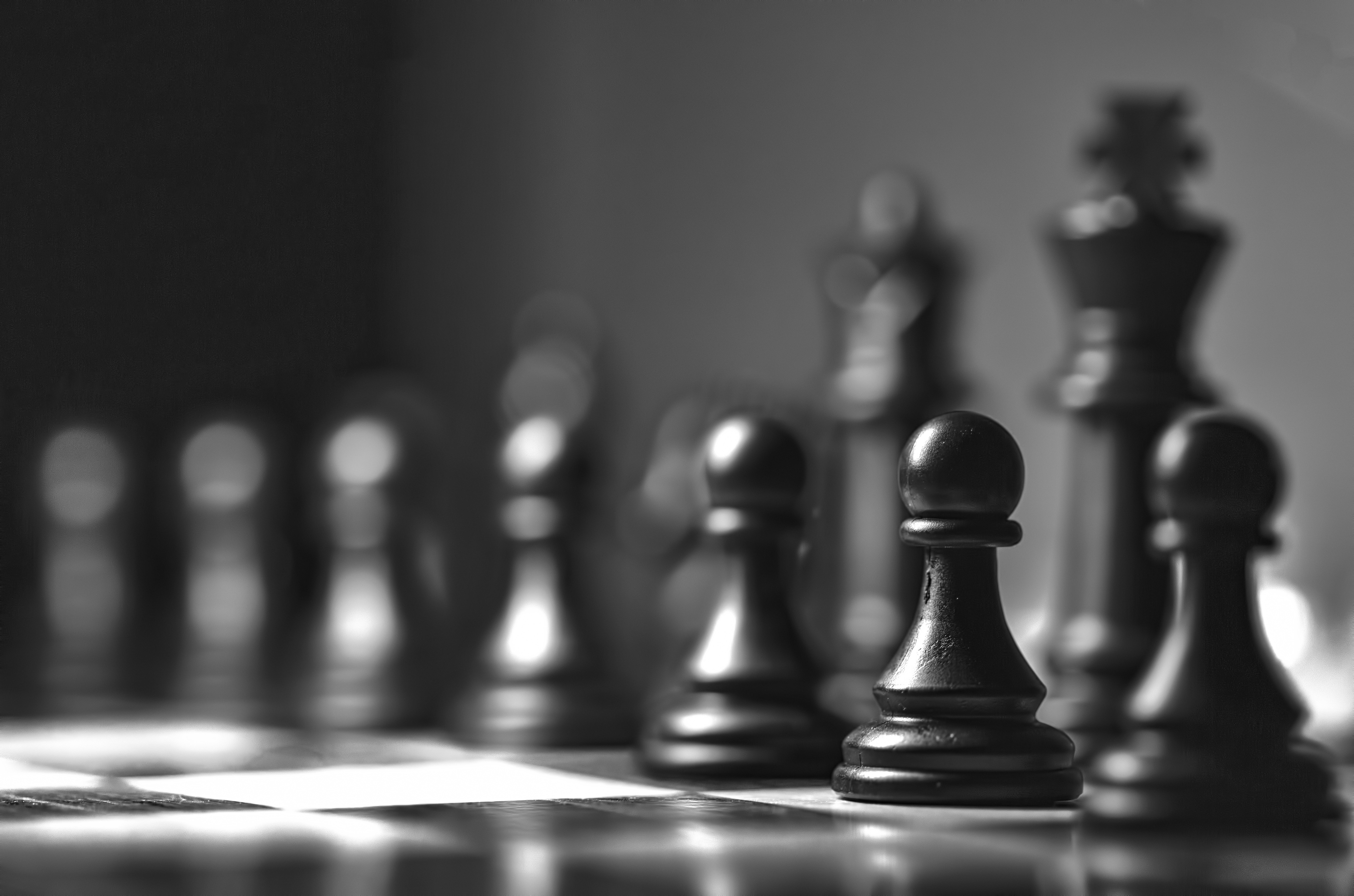 Picture of black chess pieces on a chess board in the starting position.  The image is grayscale.  Pieces in the foreground are clear, pieces furthe back are blurred.