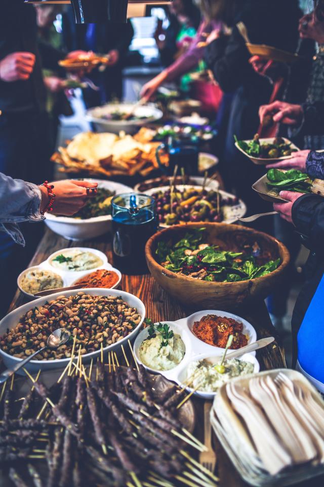 A photo of a long table crowded with dishes of food, with many hands serving themselves.