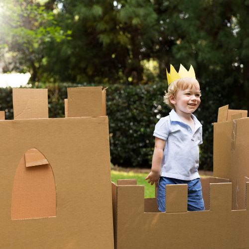 child with paper crown stands in cardboard box castle