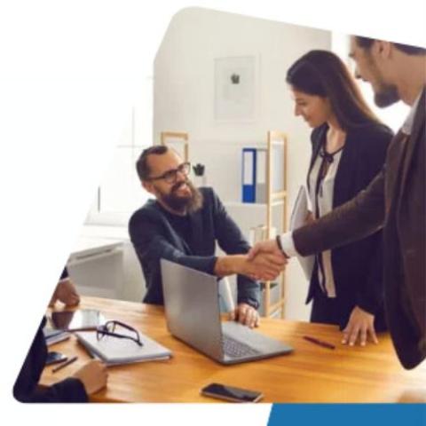 small business owner sits at laptop & shakes hands with a colleague