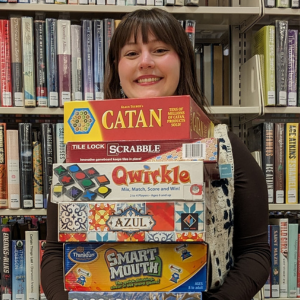 Photo of a smiling woman holding a large stack of board games. 