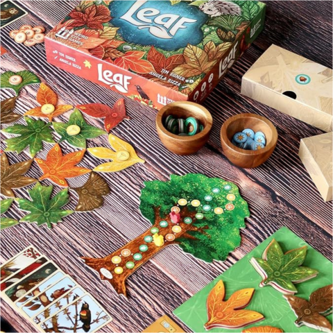 A photo of the board game Leaf, including leaf tiles, a cardboard tree with tracks, and wooden bowls of tokens. 