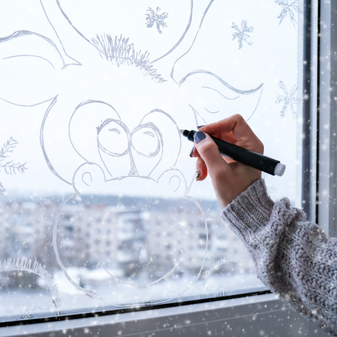 A hand holding a paint marker draws a moose on a window