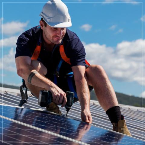 man in hardhat on roof attaches solar panel with power tool