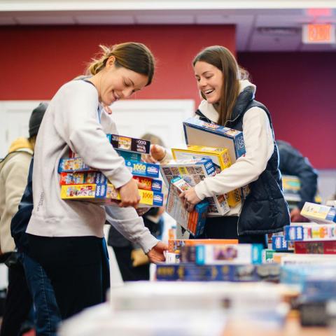 two women hold armloads of puzzles