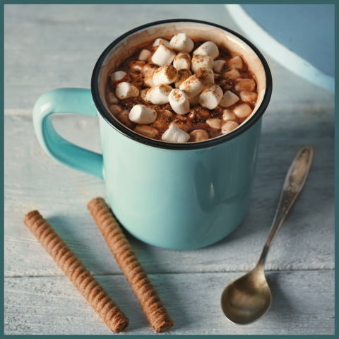 a cup of cocoa sits next to a spoon and cookies