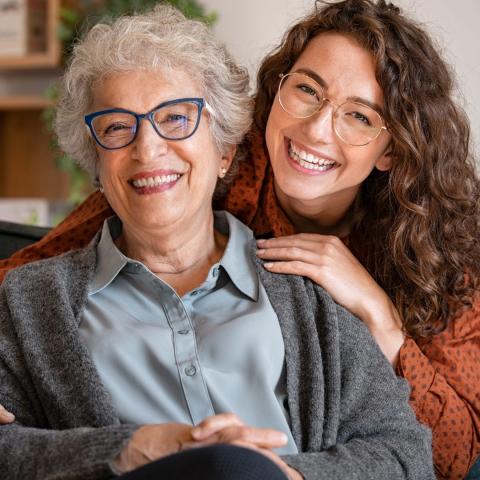 senior with grey hair and glasses smiles next to young adult with glasses