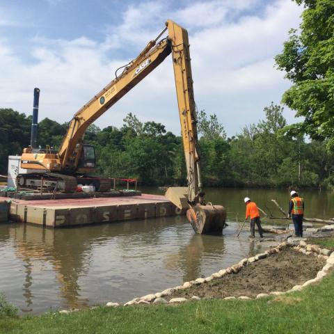 construction bucket loader scoops from lake with workers in foreground