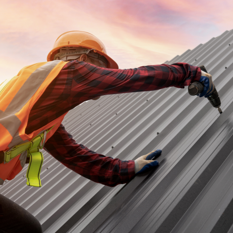 Man using a tool on a large industrial roof, sunset in the background