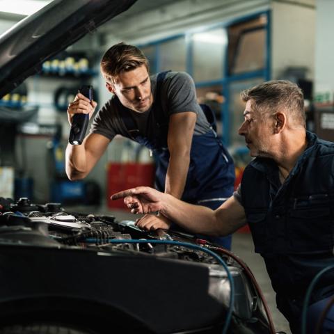 two mechanics work under the hood of a vehicle