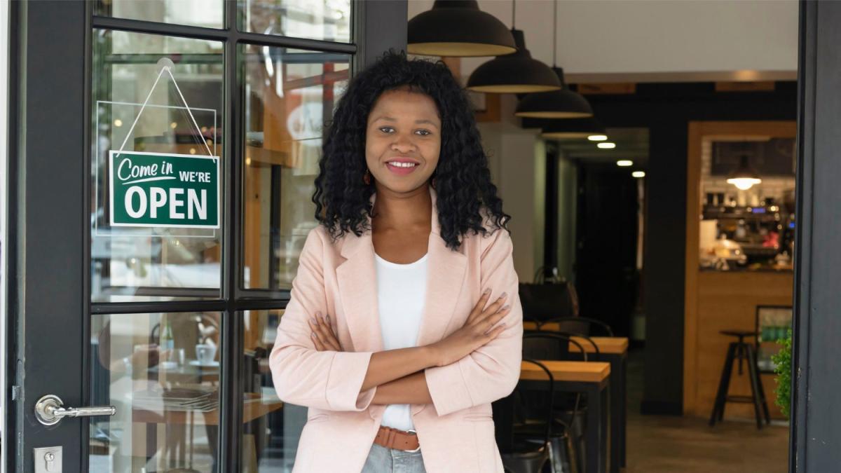 small business owner stands by door with "open" sign